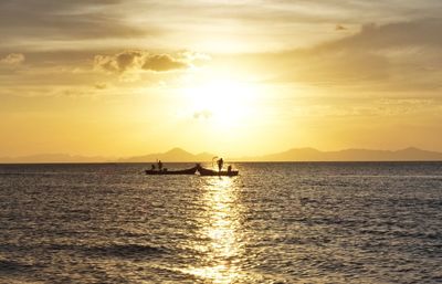 People sailing in sea against sky during sunset