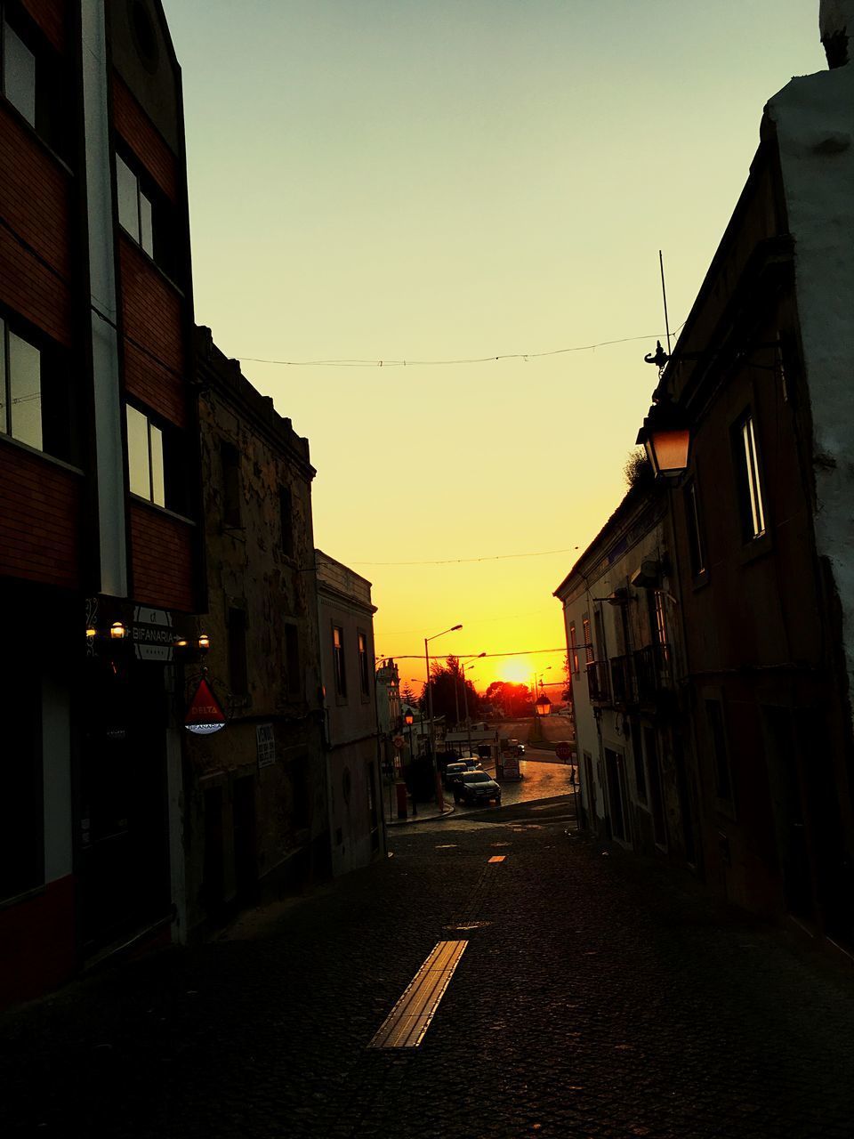 STREET AMIDST BUILDINGS IN CITY AGAINST SKY DURING SUNSET