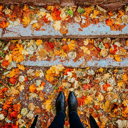 Woman in black boots standing in front of steps covered in autumn leaves 