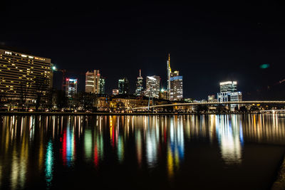 Illuminated buildings by river against sky at night