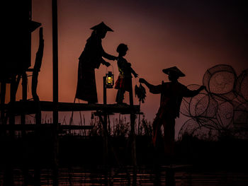 Silhouette men standing against orange sky