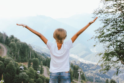 Rear view of boy with arms raised standing on mountain