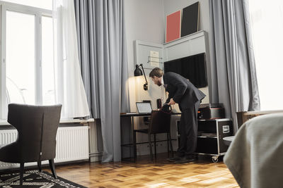 Businessman using laptop on desk standing in hotel room