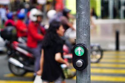 Close-up of button with arrow sign and people on road