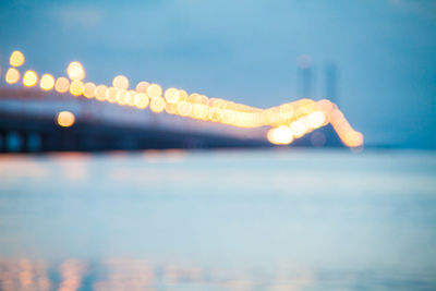 Defocused image of illuminated lights in sea against sky