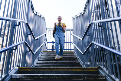 Non-binary person with disposable coffee cup using smart phone on steps