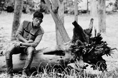 Portrait of young man sitting on tree trunk 