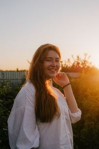 Smiling young woman standing against sky during sunset