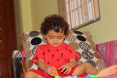 A beautiful little indian child sitting on a sofa inside the house playing with plastic toys