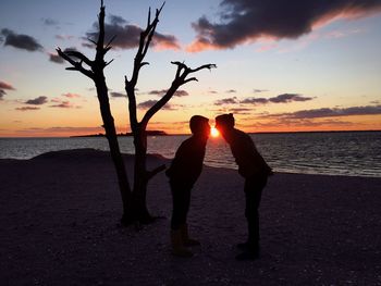 Silhouette friends on beach against sky during sunset