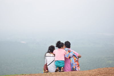 Rear view of people sitting on mountain against sky