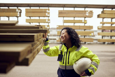 Smiling female worker examining planks stacked at lumber industry