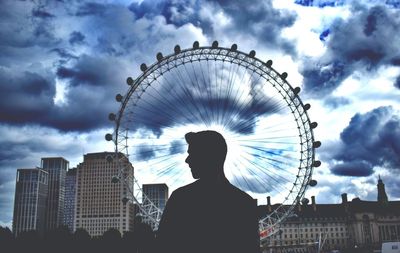 Rear view of silhouette man and ferris wheel against buildings