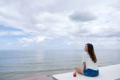 Rear view of woman sitting against sea an sky