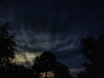 Low angle view of silhouette trees against storm clouds