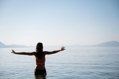 Rear view of woman standing in sea against sky