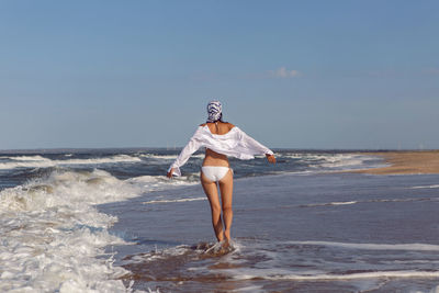 Woman run in a white bathing suit and hat sunglasses on an empty sandy beach