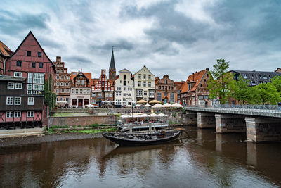 Bridge over river by buildings against cloudy sky