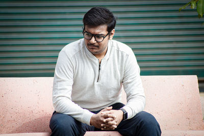 Young man looking away while sitting in city