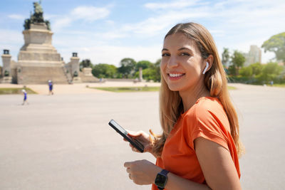 Young woman choosing the playlist on the smartphone looking at camera in sao paulo city park, brazil