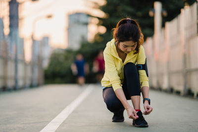 Full length of woman tying shoelace while crouching on land in city