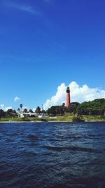 Lighthouse by sea against blue sky