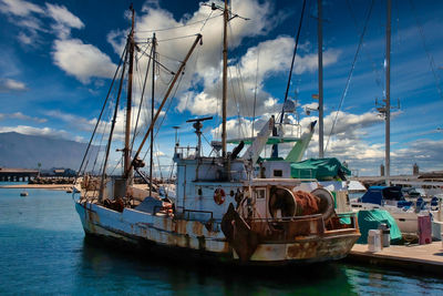 Fishing boats moored at harbor against sky