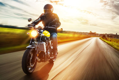 Man riding motorcycle on road against cloudy sky