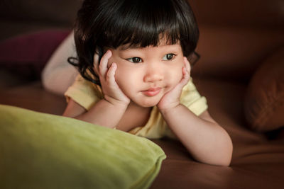 Close-up of cute baby girl with hands on chin at bed