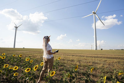 Woman, tablet in field sunflowers studies wind turbines for production of green energy, wind turbine