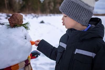 Boy in hat makes snowman, which was the nose of snowman, smiling. winter family weekend, lifestyle