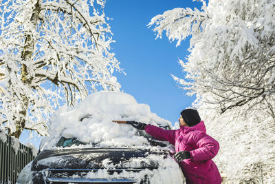 Man in knit hat cleaning snow with shovel on car