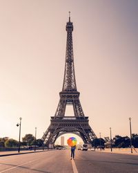 Person with colorful umbrella standing against eiffel tower in city against sky