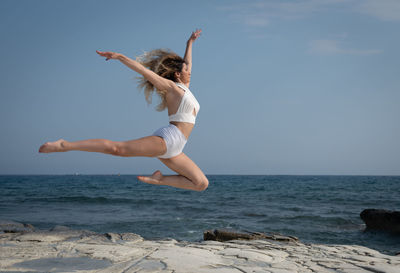 Woman jumping in sea against sky