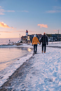 Rear view of people walking on shore against sky during sunset