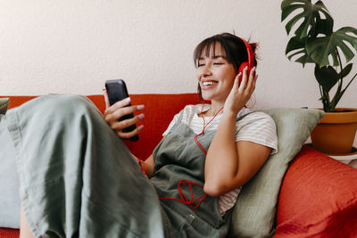 Smiling young woman using mobile phone while sitting on sofa
