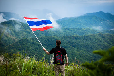 Man with flag standing on field against mountains