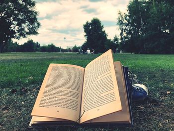 Close-up of open book on field against trees in park