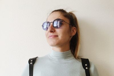 Portrait of young woman wearing sunglasses against wall