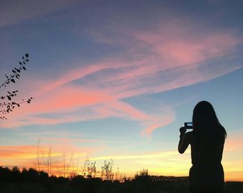 Silhouette man photographing against sky during sunset