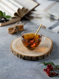 A glass cup of tea with a golden spoon and a book on a gray table