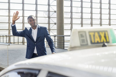 Smiling young businessman with arm raised hailing taxi