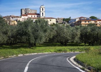 Road by houses in town against sky
