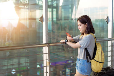 Side view of young woman standing by glass