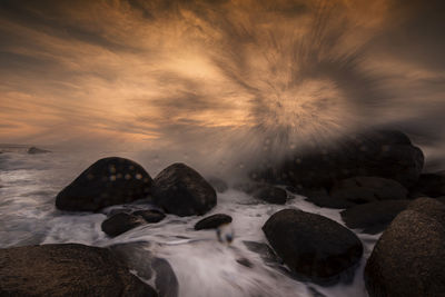 Rocks on beach against sky during sunset