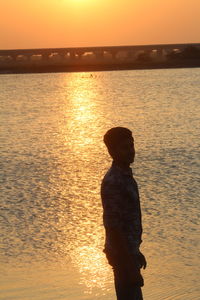Silhouette man looking at sea against sky during sunset
