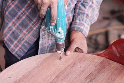 Midsection of carpenter drilling wood at workshop