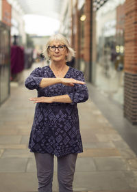 Portrait of woman gesturing while standing on footpath against buildings