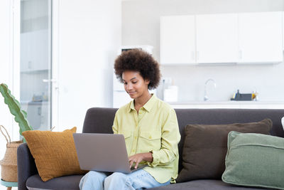 Young woman using laptop while sitting on sofa at home