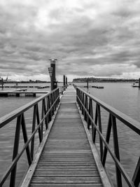 Boardwalk leading to sea against cloudy sky